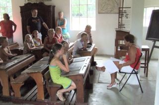 Kinderen in ouderwetse schoolbanken, met juf voor de klas